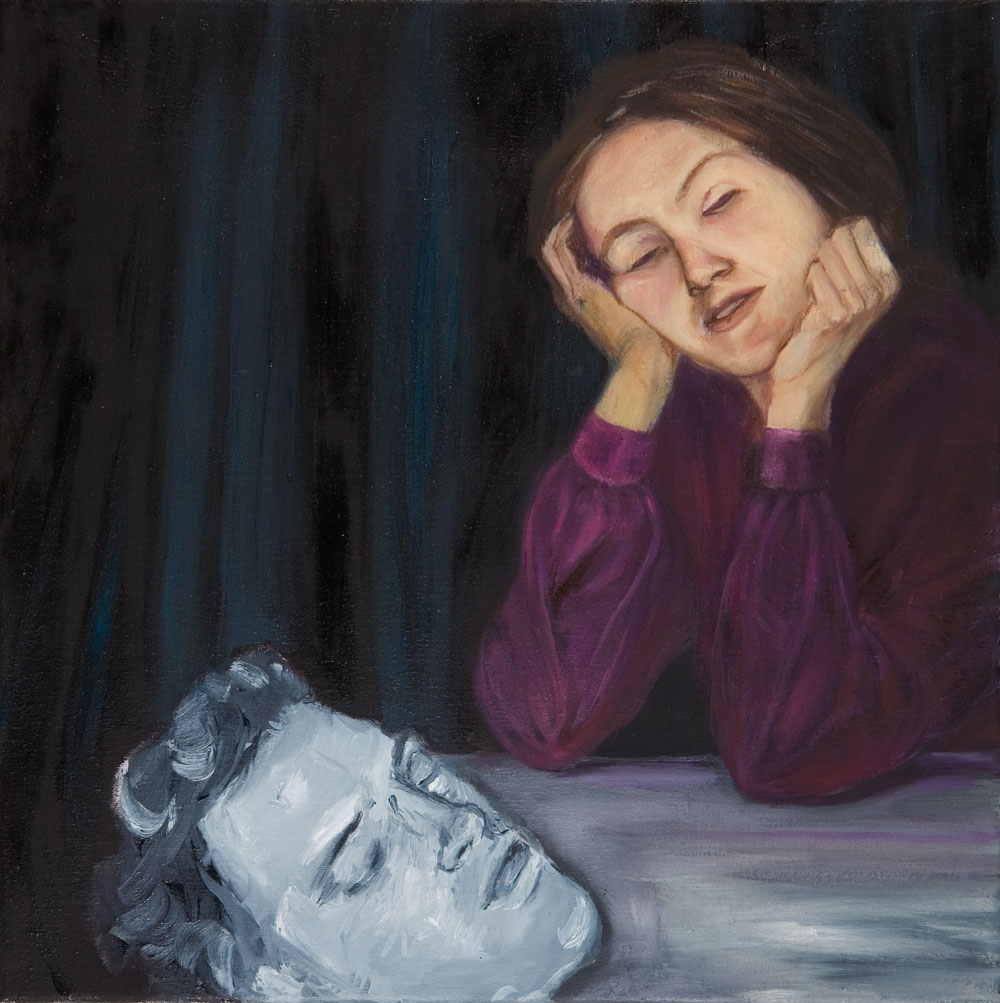 Frau mit geschlossenen Augen am Tisch, vor ihr liegt ein grauer männlicher Kopf