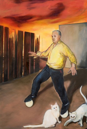 Mann in schwarzen Hosen und gelbem Hemd balanciert auf zwei Bälllen während zwei weisse Katzen um seine Beine streichen